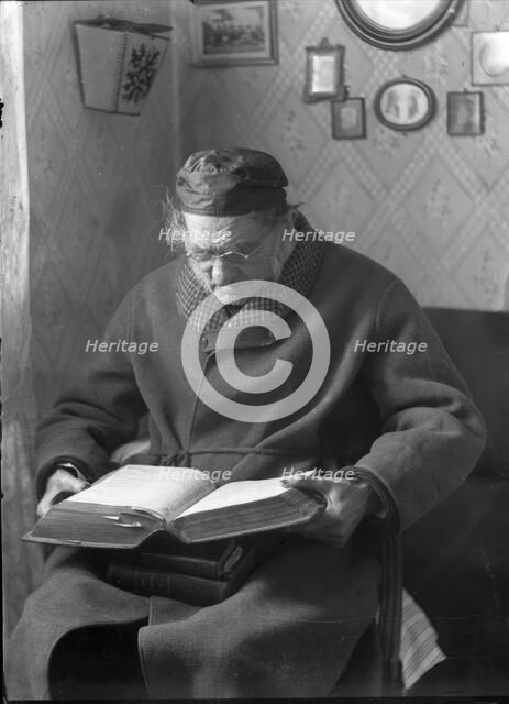 An elderly man sits and reads a book, 1880-1910. Creator: Johan Severin Nilson.