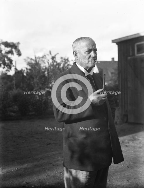 An elderly man with a starched collar, smoking a pipe in his garden, Flyinge, Sweden, 1920s. Creator: Unknown.