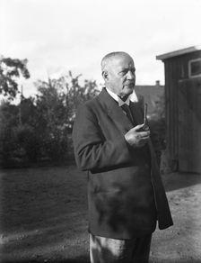 An elderly man with a starched collar, smoking a pipe in his garden, Flyinge, Sweden, 1920s. Creator: Unknown