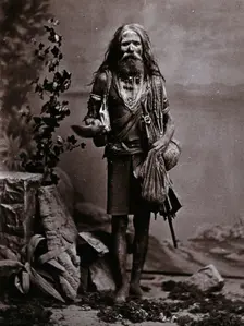 An Indian man wearing many beads, and carrying a begging bowl and an umbrella, in a..., c1900. Creator: Unknown