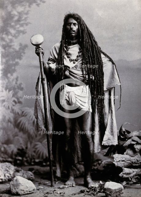 An Indian man with long hair, carrying a staff, in a studio setting, 1900. Creator: Unknown.