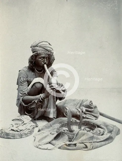 An Indian snake charmer squatting down playing his pipe, with two cobras in a basket in..., c1900. Creator: Unknown.