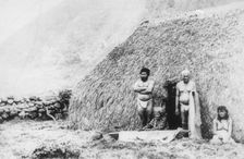 An old woman beating tapa in front of a pili grass house, Kalaupapa, Hawaii, 19th century