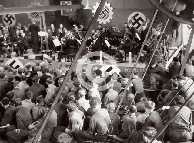 An orchestra plays to some factory workers as they take a break from work, Germany, 1936. Artist: Unknown