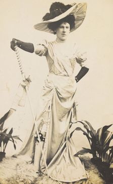 An man in drag is wearing a revealing dress and holding a staff, posing with his..., 1909. Creator: Unknown
