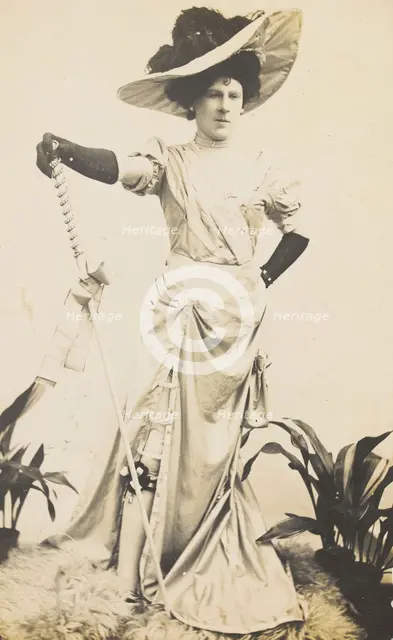 An man in drag is wearing a revealing dress and holding a staff, posing with his..., 1909. Creator: Unknown.
