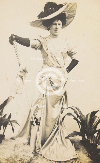 An man in drag is wearing a revealing dress and holding a staff, posing with his..., 1909. Creator: Unknown.