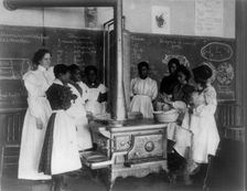 African American schoolgirls with teacher, learning to cook on a wood stove in classroom, (1899?). Creator: Frances Benjamin Johnston