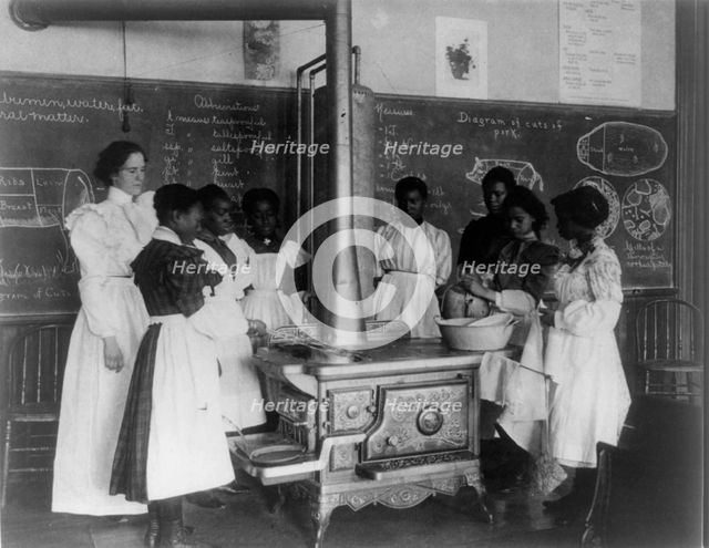 African American schoolgirls with teacher, learning to cook on a wood stove in classroom, (1899?). Creator: Frances Benjamin Johnston.