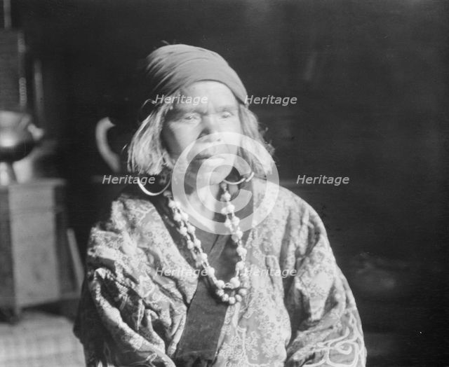 Ainu woman wearing a headscarf, earrings, and a necklace, 1908. Creator: Arnold Genthe.