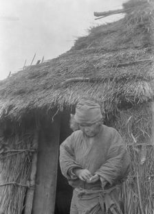 Ainu woman outside a hut, 1908. Creator: Arnold Genthe