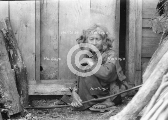 Ainu woman seated by the door of a wooden hut, 1908. Creator: Arnold Genthe.