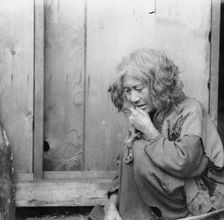 Ainu woman seated by the door of a wooden hut, 1908. Creator: Arnold Genthe