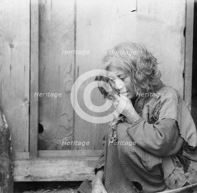 Ainu woman seated by the door of a wooden hut, 1908. Creator: Arnold Genthe.