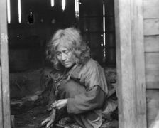 Ainu woman seated in the doorway of a wooden hut, 1908. Creator: Arnold Genthe
