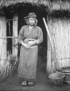 Ainu woman standing by the doorway of a hut, 1908. Creator: Arnold Genthe