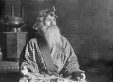 Ainu chief wearing a headdress seated with a sword in his lap, 1908. Creator: Arnold Genthe