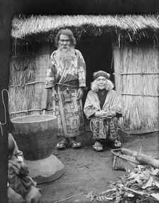 Ainu man and seated woman at the entrance of a hut, 1908. Creator: Arnold Genthe
