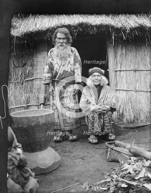 Ainu man and seated woman at the entrance of a hut, 1908. Creator: Arnold Genthe.