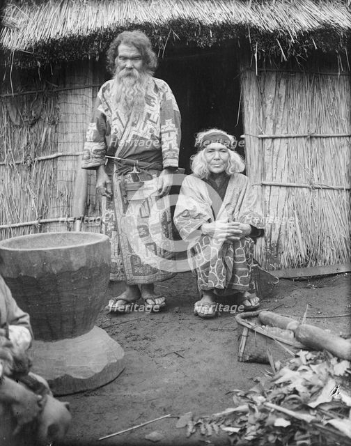 Ainu man and seated woman at the entrance of a hut, 1908. Creator: Arnold Genthe.