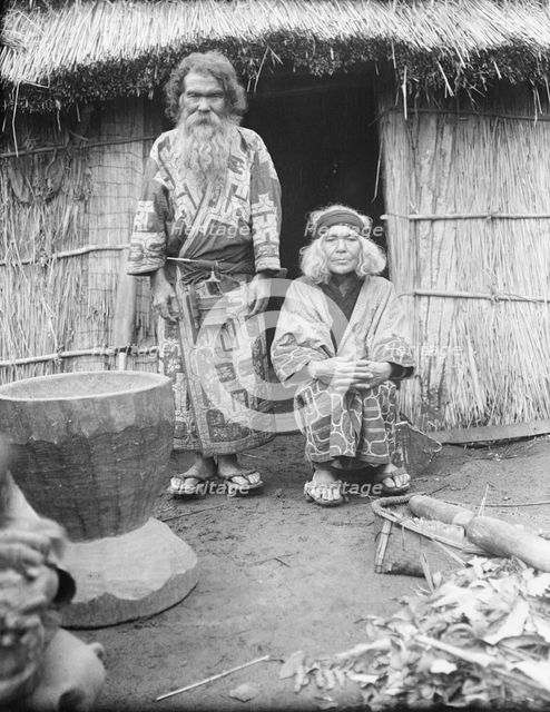 Ainu man and seated woman at the entrance of a hut, 1908. Creator: Arnold Genthe.