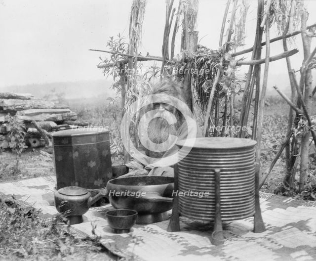 Ainu man seated outdoors on a mat covered with clay containers, 1908. Creator: Arnold Genthe.