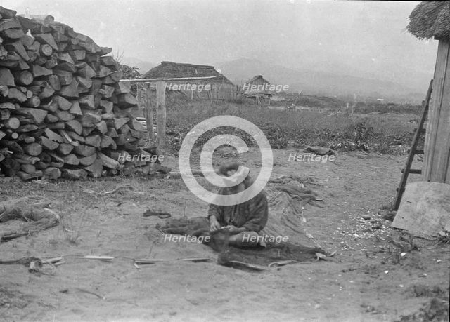 Ainu man seated outside working on nets, 1908. Creator: Arnold Genthe.