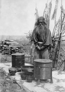 Ainu man standing outdoors on a mat covered with clay containers, 1908. Creator: Arnold Genthe
