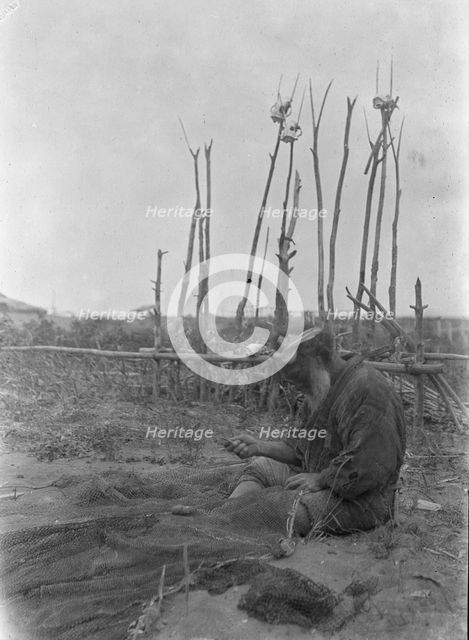 Ainu seated outside working on nets, 1908. Creator: Arnold Genthe.