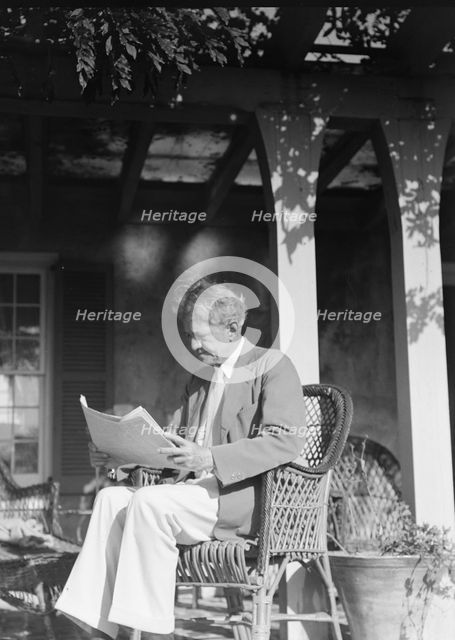 Arnold Genthe seated outdoors in a wicker chair reading, between 1911 and 1942. Creator: Arnold Genthe.