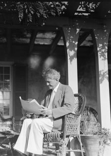 Arnold Genthe seated outdoors in a wicker chair reading, between 1911 and 1942. Creator: Arnold Genthe