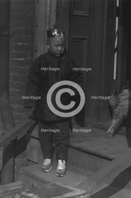 Boy standing on steps in front of a doorway, Chinatown, San Francisco, between 1896 and 1906. Creator: Arnold Genthe.