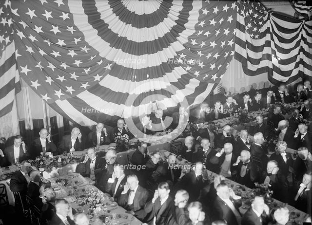 Banquet Scene with Flag Draping And Men Seated Holding Up Listening Device To One Ear, c1913-1917. Creator: Harris & Ewing.