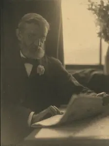Bearded man in spectacles reading a newspaper, c1900. Creator: Anne K Pilsbury