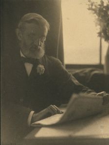 Bearded man in spectacles reading a newspaper, c1900. Creator: Anne K Pilsbury