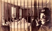 Bellevue Hospital, New York City: male patients (criminal insane?) in bed in ward, prison bars in... Creator: Unknown
