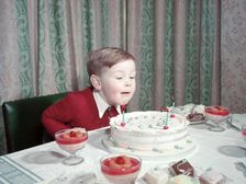 Birthday boy blowing out the candles on his cake, c1955. Creator: Arthur Charles Kirby Ware