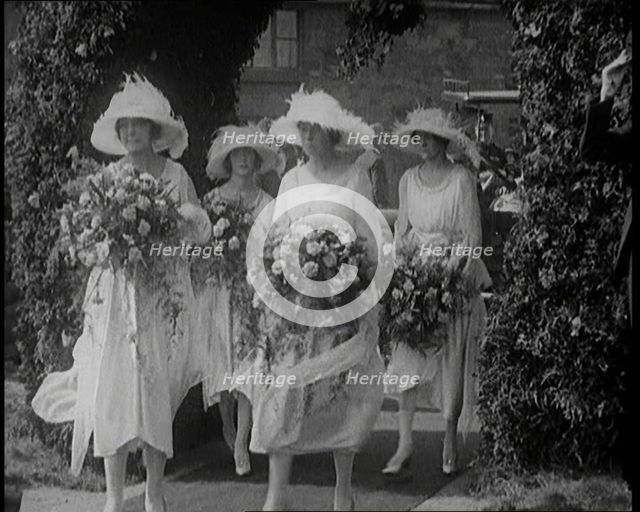 British Bridesmaids Walking Through a Flowery Arch, Holding Flowers, 1921. Creator: British Pathe Ltd.