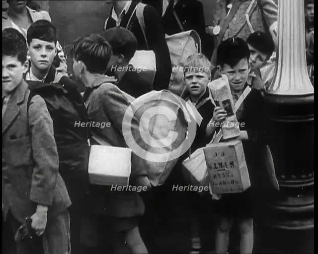 British Child Evacuees Standing on a Pavement With Bags and Boxes as Adults are Standing..., 1939. Creator: British Pathe Ltd.