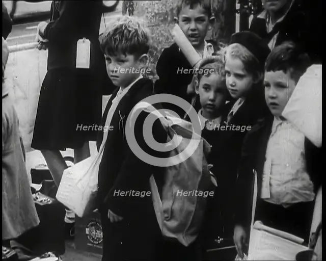 British Child Evacuees Standing on a Pavement With Bags and Boxes as Adults are Standing..., 1939. Creator: British Pathe Ltd.