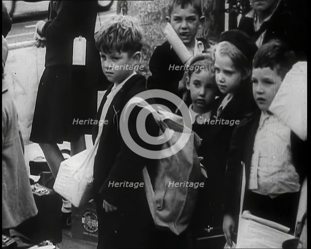 British Child Evacuees Standing on a Pavement With Bags and Boxes as Adults are Standing..., 1939. Creator: British Pathe Ltd.