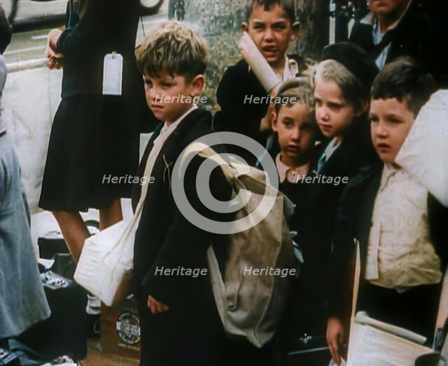 British Child Evacuees Standing on a Pavement With Bags and Boxes as Adults are Standing..., 1939. Creator: British Pathe Ltd.