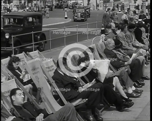 British Holidaymakers Sitting on Deckchairs on the Promenade at Brighton and Cars Driving..., 1938. Creator: British Pathe Ltd.