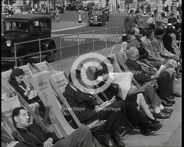 British Holidaymakers Sitting on Deckchairs on the Promenade at Brighton and Cars Driving..., 1938. Creator: British Pathe Ltd.