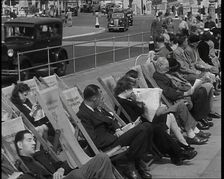 British Holidaymakers Sitting on Deckchairs on the Promenade at Brighton and Cars Driving..., 1938. Creator: British Pathe Ltd