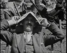 British Man in a Three Piece Suit Sitting in a Deckchair Smiling at the Camera and Holding..., 1938. Creator: British Pathe Ltd