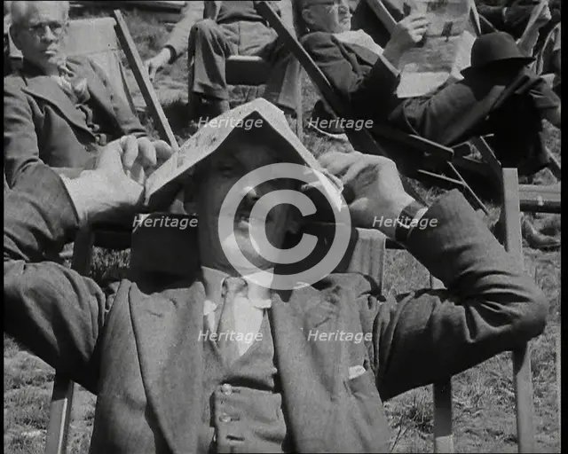 British Man in a Three Piece Suit Sitting in a Deckchair Smiling at the Camera and Holding..., 1938. Creator: British Pathe Ltd.