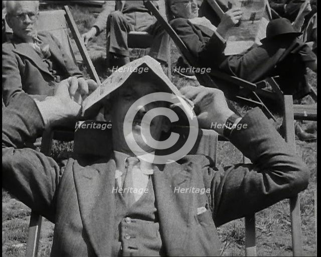 British Man in a Three Piece Suit Sitting in a Deckchair Smiling at the Camera and Holding..., 1938. Creator: British Pathe Ltd.