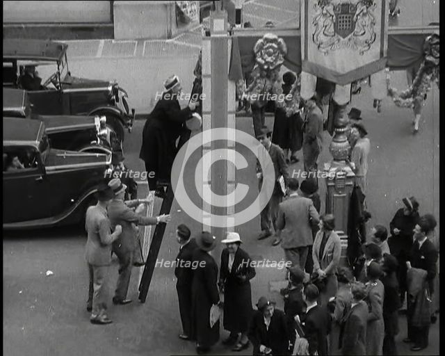 Bud Flanagan With a Frying Pan Climbing a Ladder Resting Against Coronation Decorations in..., 1937. Creator: British Pathe Ltd.