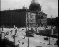 Bus Driving Down a Wide Road with a Large Building in the Background, 1933. Creator: British Pathe Ltd